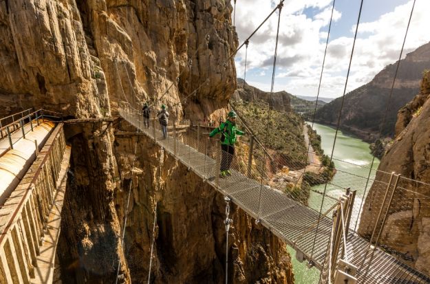 Three tourist walking by one of Caminito del Rey's bridge